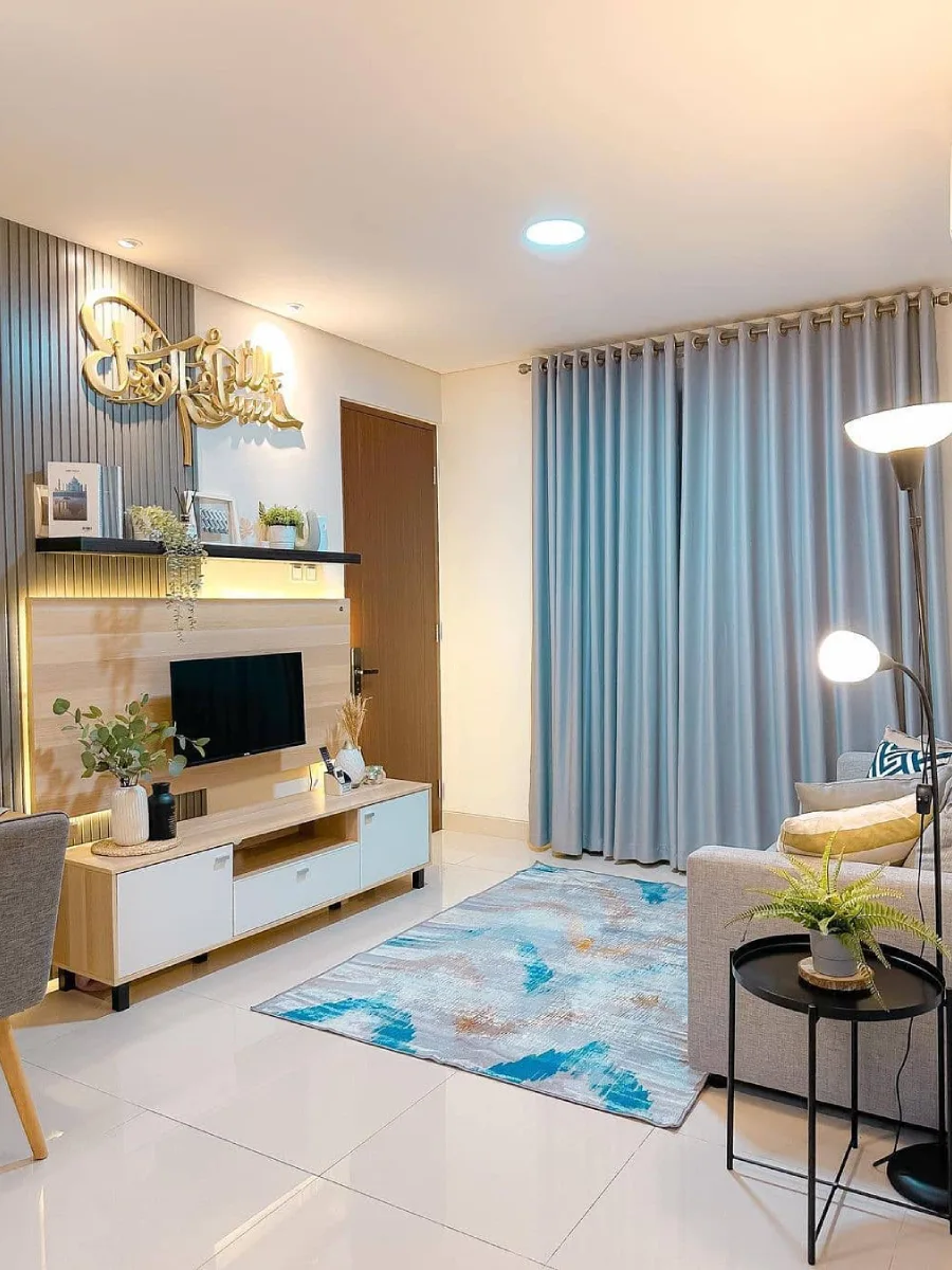 Desain ruang keluarga modern dengan backdrop TV panel kayu, hiasan kaligrafi emas, gorden biru muda, dan karpet abstrak minimalis.