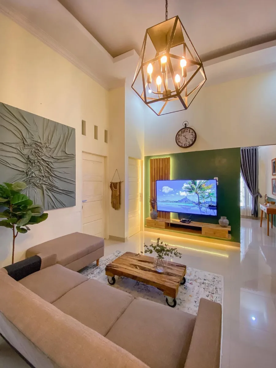 Desain ruang keluarga plafon tinggi dengan lampu gantung industrial, dinding aksen hijau gelap, dan karya seni dinding 3D yang artistik.