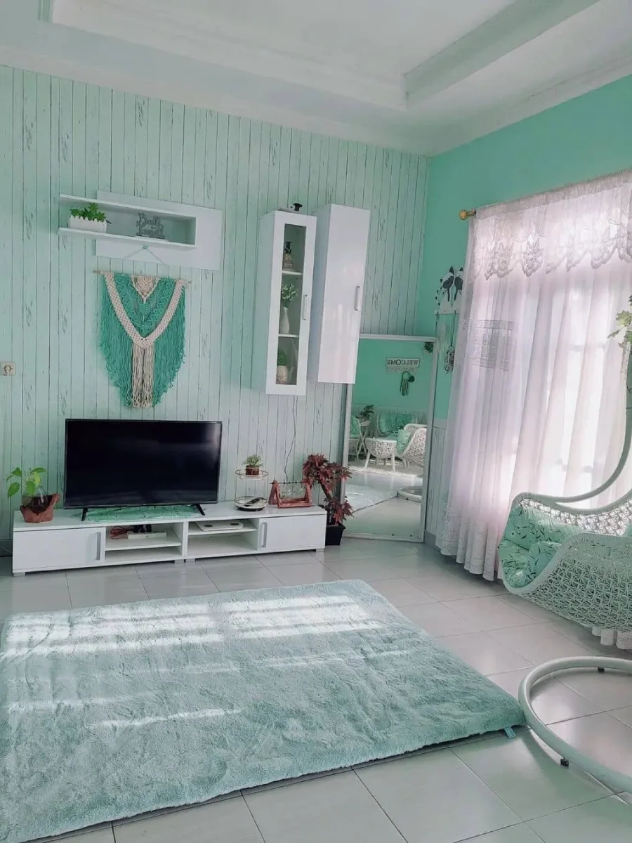 Ruang santai bertema mint dengan dinding motif kayu, hiasan makrame, dan kursi gantung rotan untuk suasana santai.