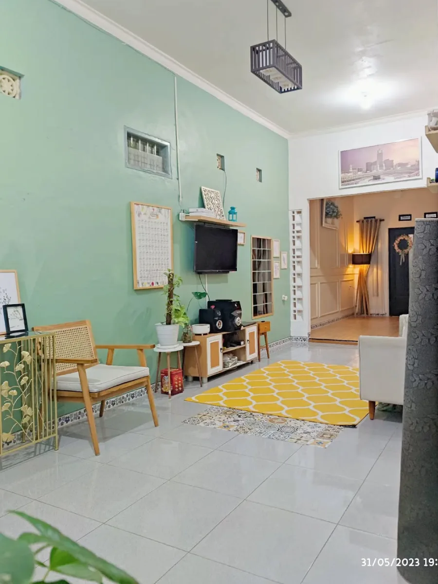 Sudut ruang menonton dengan karpet kuning bermotif, dinding hijau, dan lantai keramik dengan kombinasi tegel kunci yang unik.