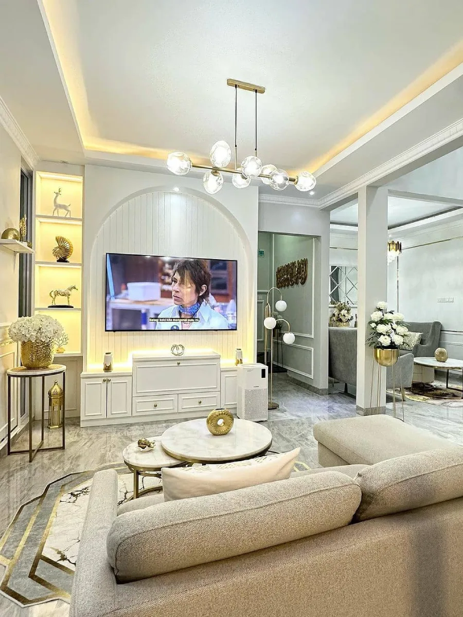 Desain ruang keluarga mewah minimalis dengan aksen emas, meja marmer bertingkat, dan dinding TV berbentuk lengkungan yang elegan.