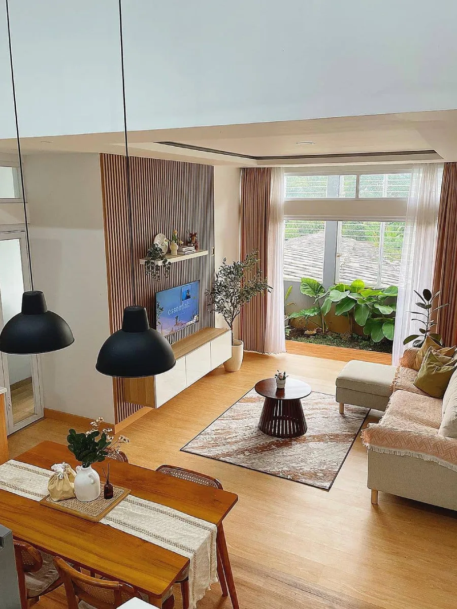 Desain ruang keluarga modern minimalis bergaya Japandi dengan panel dinding kayu, lantai parket yang hangat, jendela besar dengan pemandangan tanaman hijau, serta furnitur bergaris bersih yang menciptakan suasana tenang dan lega.