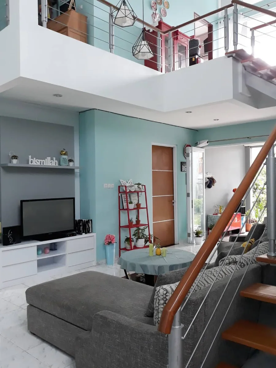 Pemandangan ruang keluarga dari arah tangga menunjukkan area mezzanine, rak tanaman merah, dan pintu kayu minimalis.