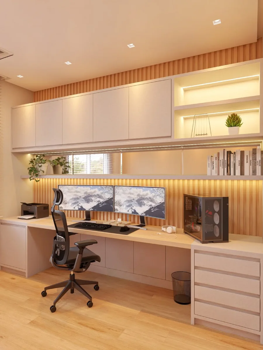 Ruang kerja di rumah bergaya modern dengan meja panjang, setup dua monitor, panel dinding wood slat kayu, dan kabinet atas berwarna krem dengan pencahayaan LED tersembunyi.