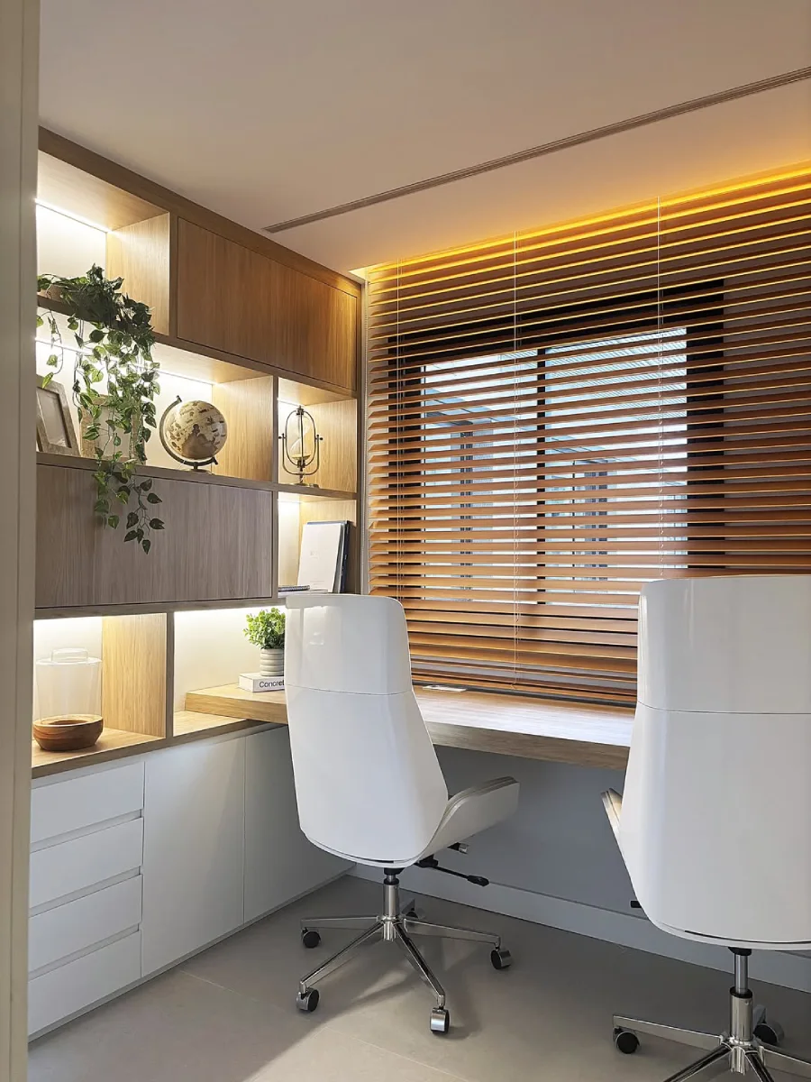 Ruang kerja terang benderang dengan meja kayu menghadap jendela berkerai kayu (wooden blinds), dua kursi putih modern, dan rak pajangan dengan lampu LED.
