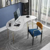 Meja kerja modern berbentuk asimetris melengkung dengan permukaan putih bermotif marmer dan kaki besi ramping berwarna emas, dilengkapi kursi biru beludru.