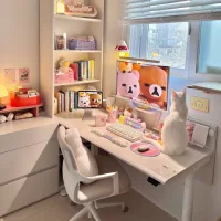 Meja kerja aestetik perempuan dengan nuansa pastel, dilengkapi monitor karakter lucu, rak buku rapi, keyboard putih, dan kucing putih di atas meja dekat jendela.
