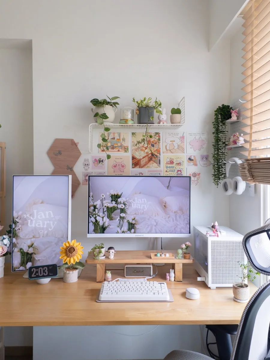 Tampak depan meja kerja wanita estetik dengan dua monitor menampilkan wallpaper bunga tulip putih, rak dinding kawat berisi tanaman hias, dan casing PC mini putih di atas meja kayu terang.