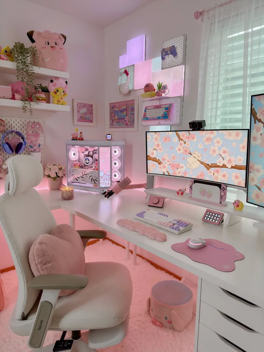 Detail close-up meja gaming pink, menyoroti perlengkapan meja seperti mousepad Ditto pink, dudukan Nintendo Switch, mikrofon pink, dan keyboard mekanikal bernuansa ungu-putih.