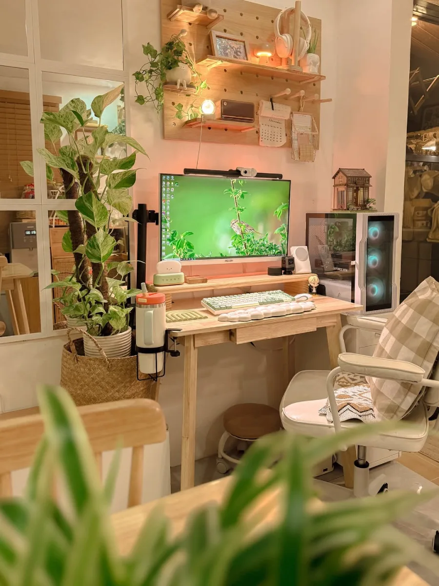 Sudut pandang lain dari meja kerja bernuansa earthy, memperlihatkan pot besar tanaman marble queen pothos di lantai sisi kiri dan kursi kerja putih berbantal motif plaid.