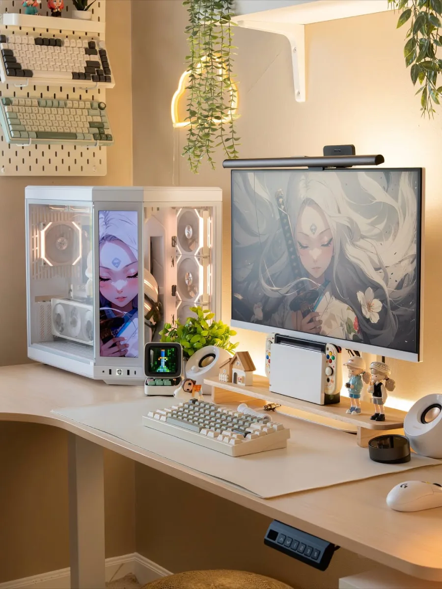 Tampilan jarak dekat meja kerja estetik dengan layar monitor utama, keyboard mekanik putih di atas desk mat, Nintendo Switch, dan dekorasi miniatur serta tanaman hias kecil yang rapi.