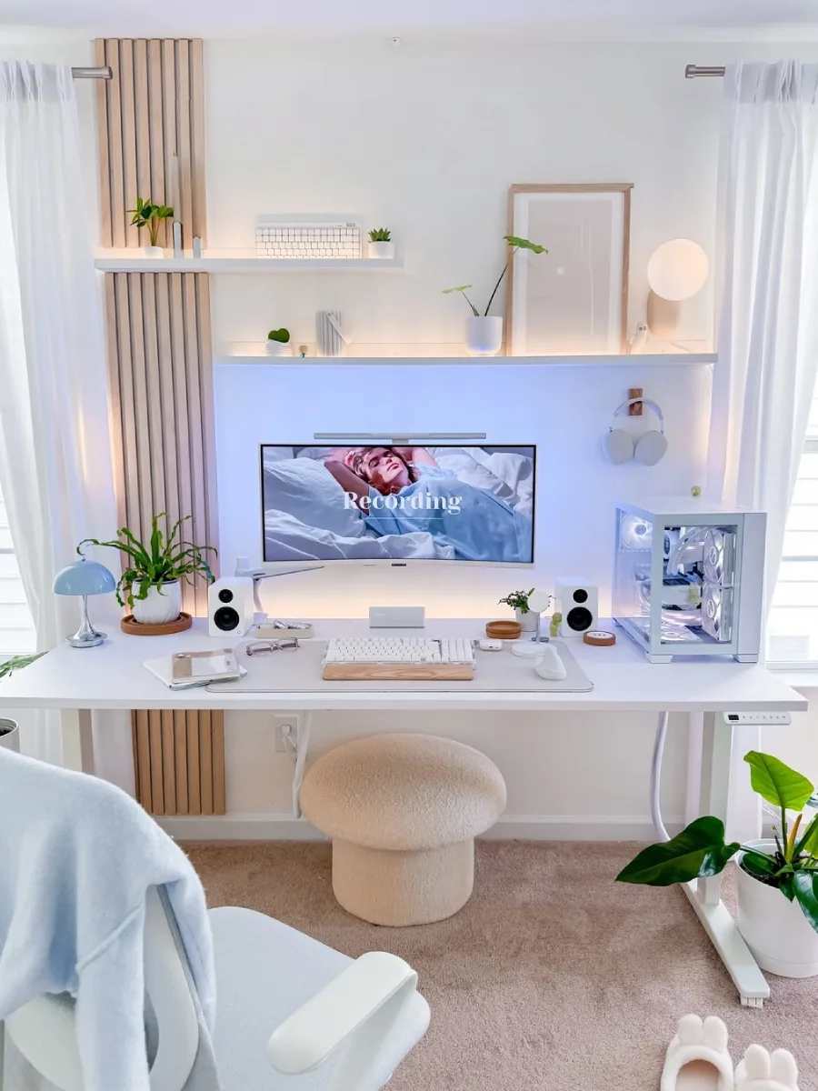 Sudut pandang depan dari meja kerja bernuansa putih dan kayu, menampilkan setup PC serba putih, monitor lengkung, keyboard estetik, dan pencahayaan alami yang lembut dari jendela di kedua sisinya.