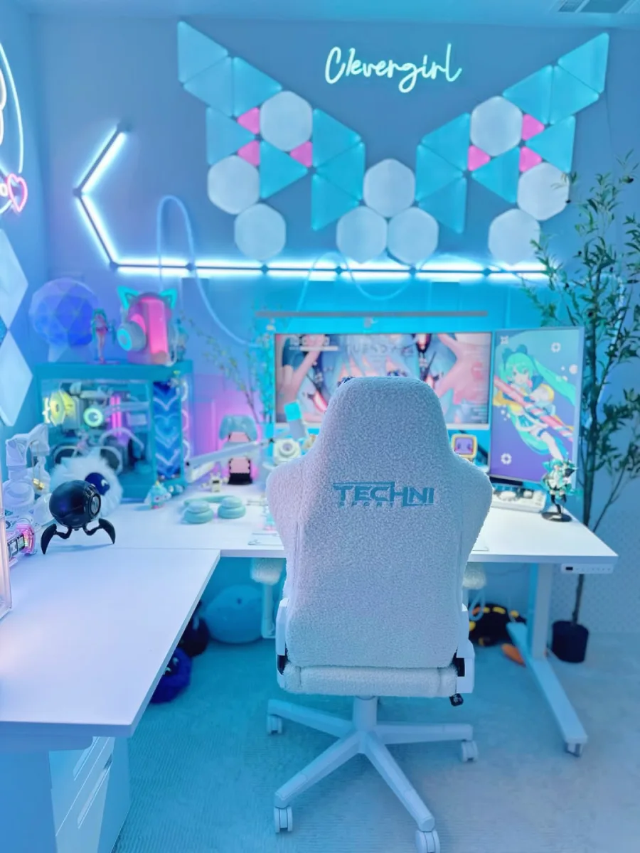 Tampak belakang kursi gaming putih berbahan fleece dengan logo Techni Sport, menghadap ke meja kerja bernuansa biru es. Terlihat setup dual monitor dengan wallpaper Hatsune Miku, keyboard mekanikal, dan PC case transparan di sebelah kiri.