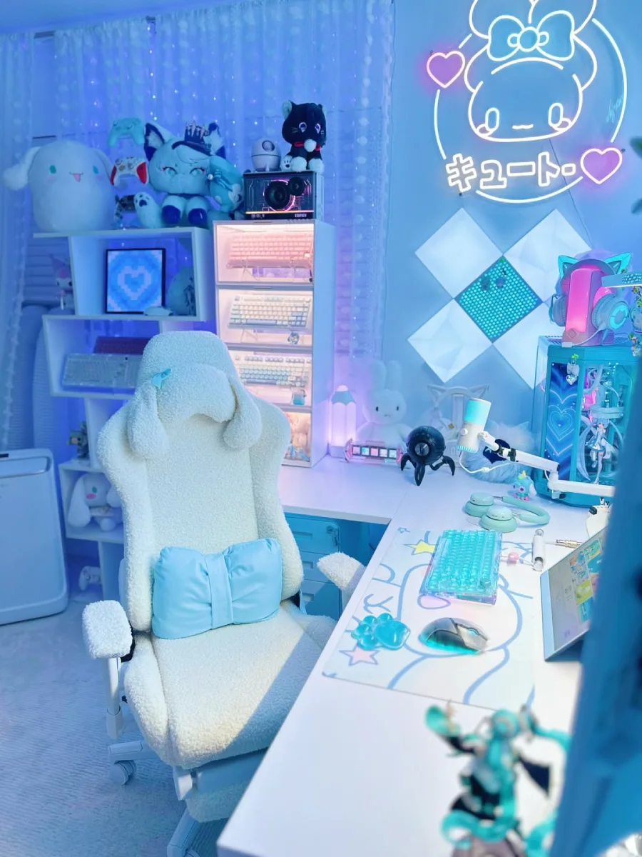 Sudut samping meja kerja gaming bernuansa biru terang. Memperlihatkan detail kursi putih berbulu dengan sandaran kepala berbentuk telinga kelinci yang lucu, serta rak putih susun di sebelah kiri yang memajang koleksi keyboard mekanikal.