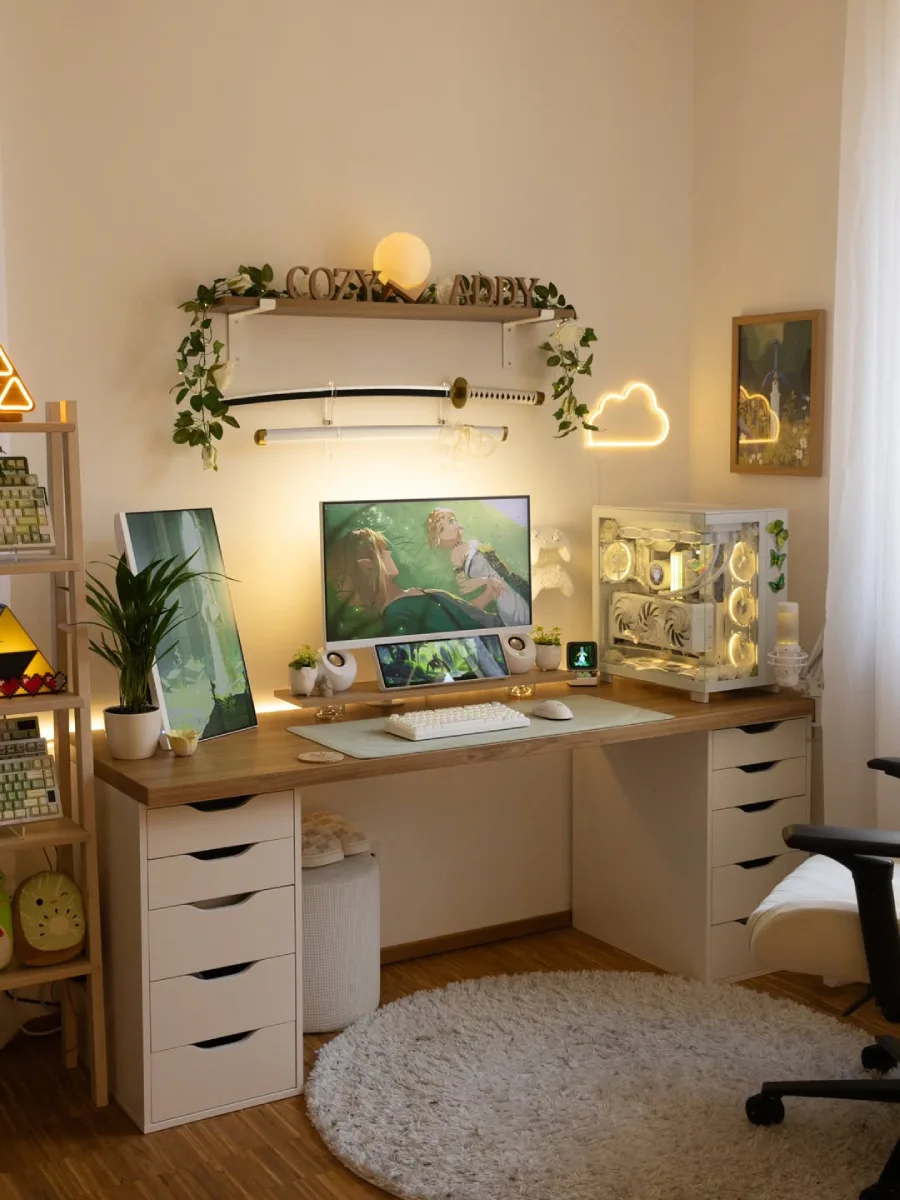 Tampilan penuh meja kerja dan area bermain game wanita yang estetik dan bernuansa hangat. Meja kayu panjang ditopang oleh dua kabinet laci berwarna putih di sisi kiri dan kanan. Di atas meja terdapat monitor utama dan layar tambahan kecil di bawahnya yang menampilkan wallpaper The Legend of Zelda, diapit oleh speaker putih, keyboard dan mouse putih, serta casing PC transparan berwarna putih dengan lampu LED kekuningan. Di dinding atas terdapat rak melayang dengan dekorasi tanaman rambat artifisial, lampu berbentuk bulan, pajangan huruf kayu 'COZY ABBEY', dan pedang katana. Sebuah lampu neon berbentuk awan menyala di dinding kanan. Di lantai kayu terdapat karpet bulu bundar berwarna putih dan sebagian kursi kerja berwarna senada.