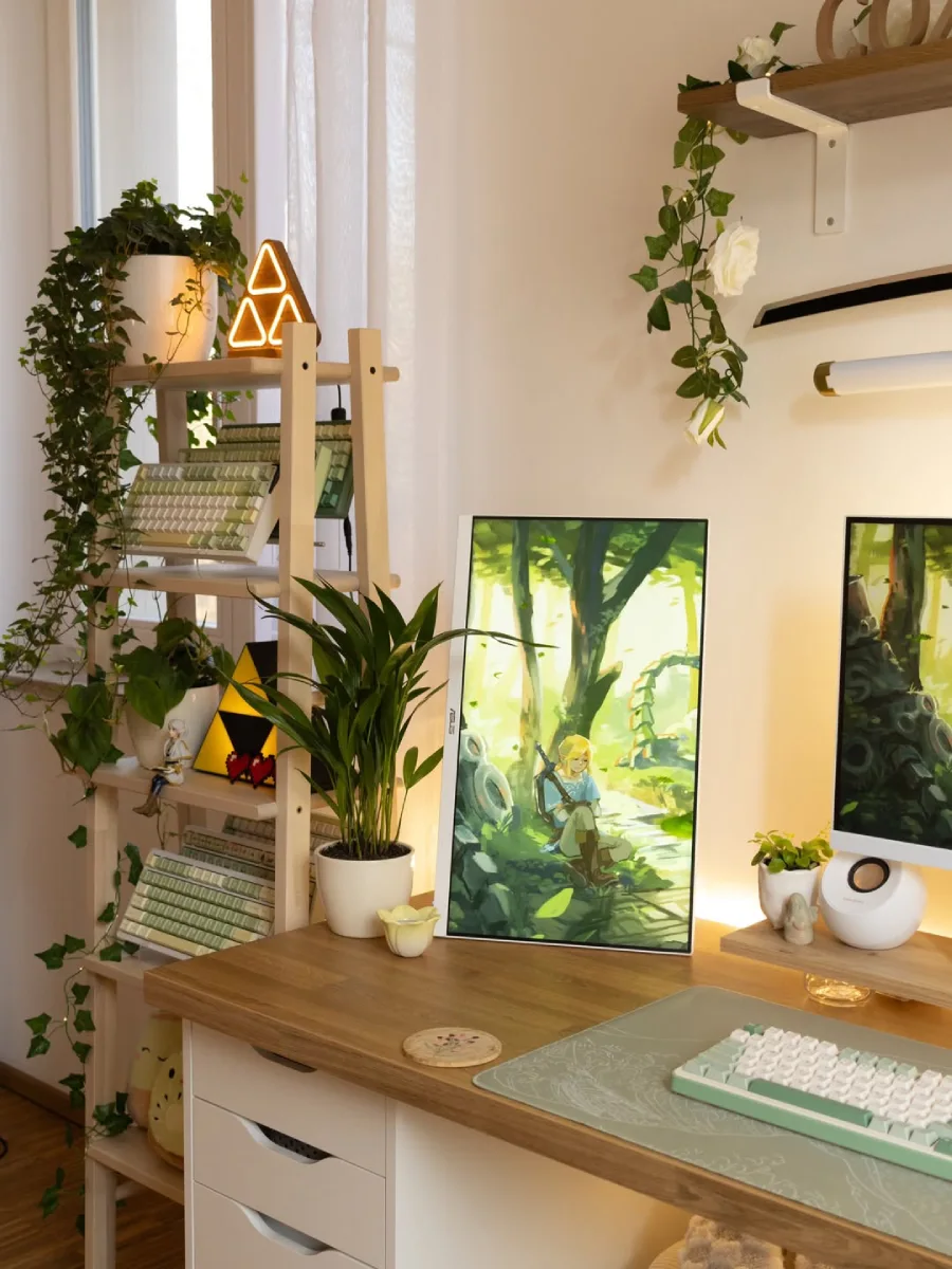 Tampilan jarak dekat sudut kiri meja kerja estetik yang berdekatan dengan rak kayu bersusun di dekat jendela. Rak kayu tersebut memajang koleksi keyboard mekanikal bernuansa hijau dan putih, beberapa tanaman hias dalam pot berbunga dan merambat, lampu hias berbentuk Triforce yang menyala, serta boneka plushie. Di atas meja kayu, terdapat sebuah monitor berposisi vertikal yang menampilkan wallpaper karakter Link dari The Legend of Zelda, diletakkan di sebelah pot tanaman hijau berdaun panjang. Di bagian depan meja, terlihat sebagian keyboard mekanikal berwarna hijau-putih di atas desk mat (alas meja) bercorak senada.