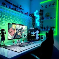 Setup meja gamer modern dengan lampu LED hijau biru, monitor menampilkan karakter anime, PC RGB transparan, panel dinding 3D, dan rak koleksi figure di sudut ruangan.