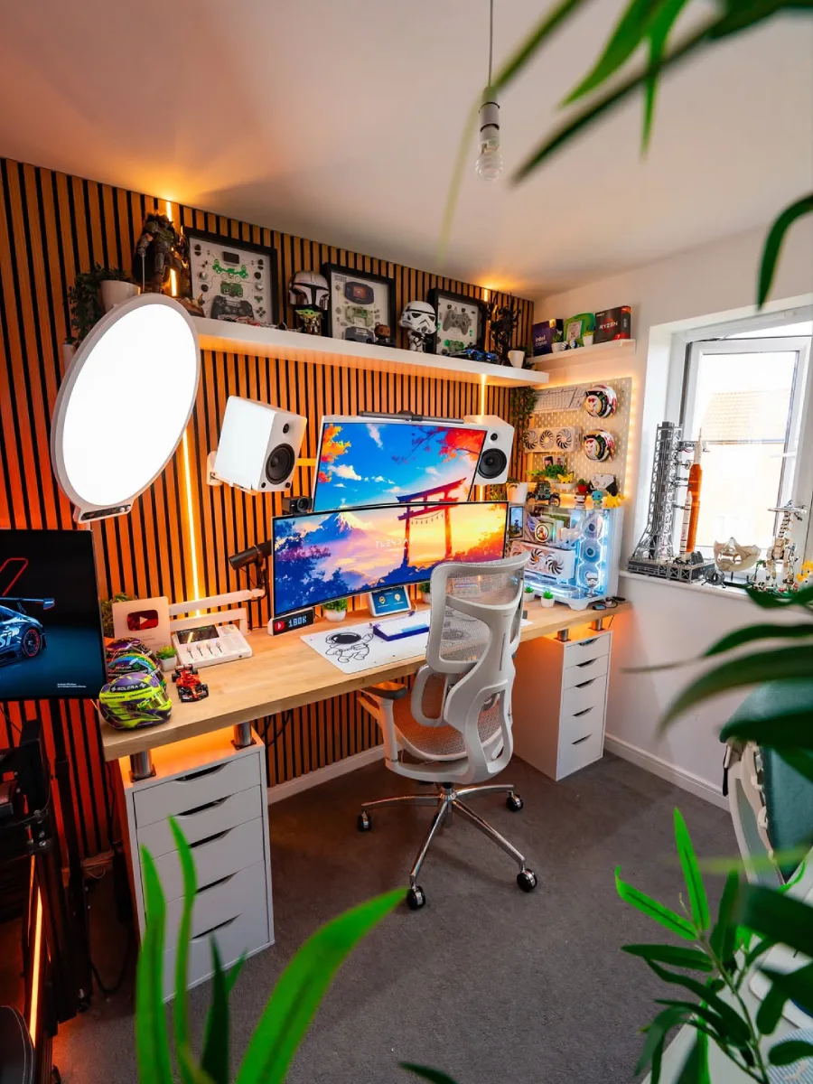 Setup PC dengan dinding panel kayu berlampu latar oranye hangat. Terdapat dua monitor ditumpuk secara horizontal dan satu monitor vertikal di kiri, casing PC transparan berwarna putih, speaker putih, kursi ergonomis putih, serta rak yang penuh dengan helm miniatur dan koleksi Star Wars.