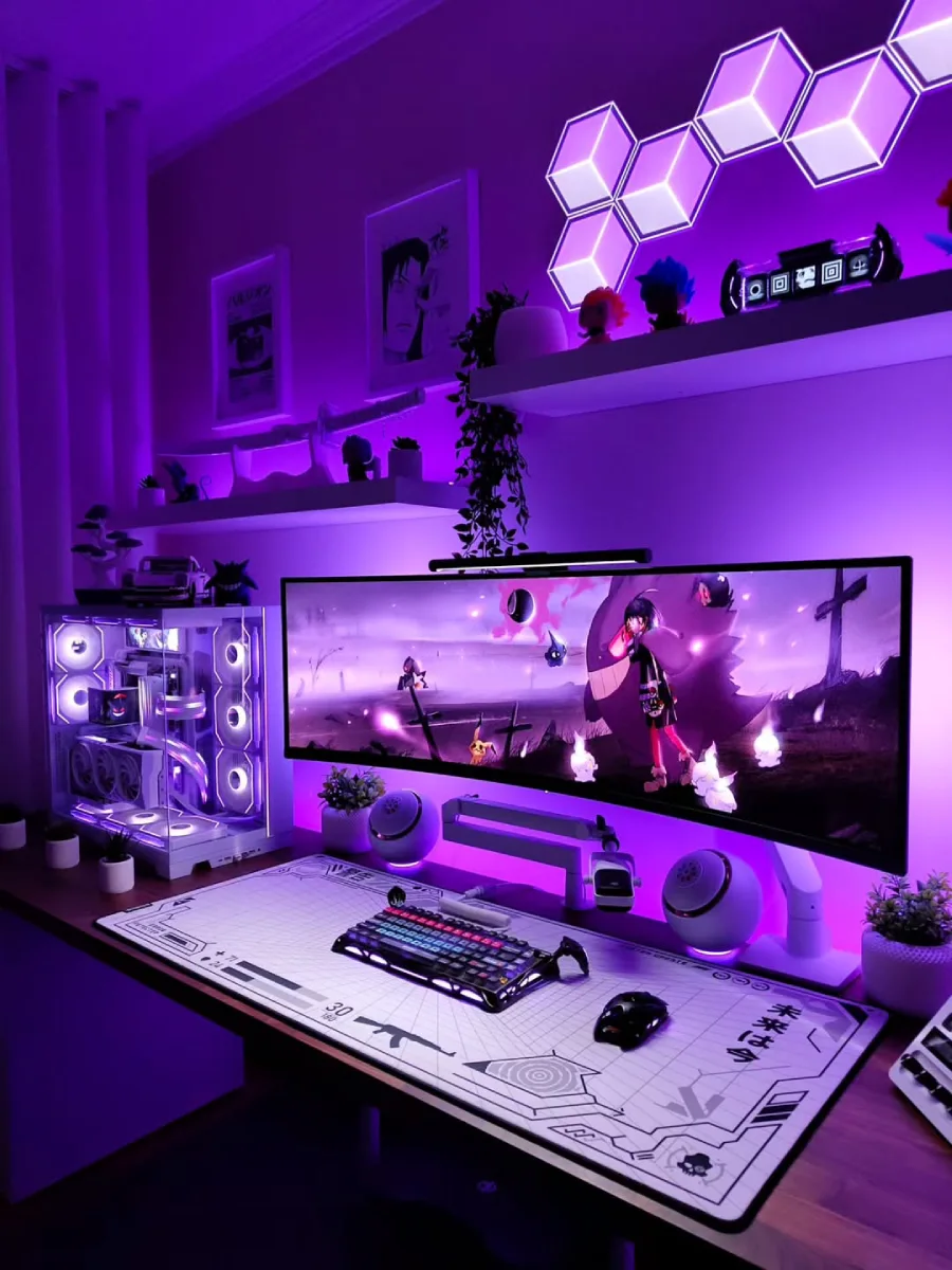 Setup PC yang sama dengan nuansa ungu pekat. Layar super ultrawide menampilkan wallpaper anime bernuansa gelap. Di atas meja kayu terdapat keyboard mekanikal hitam, mouse hitam, speaker bulat, dan casing PC transparan bernuansa putih-ungu.