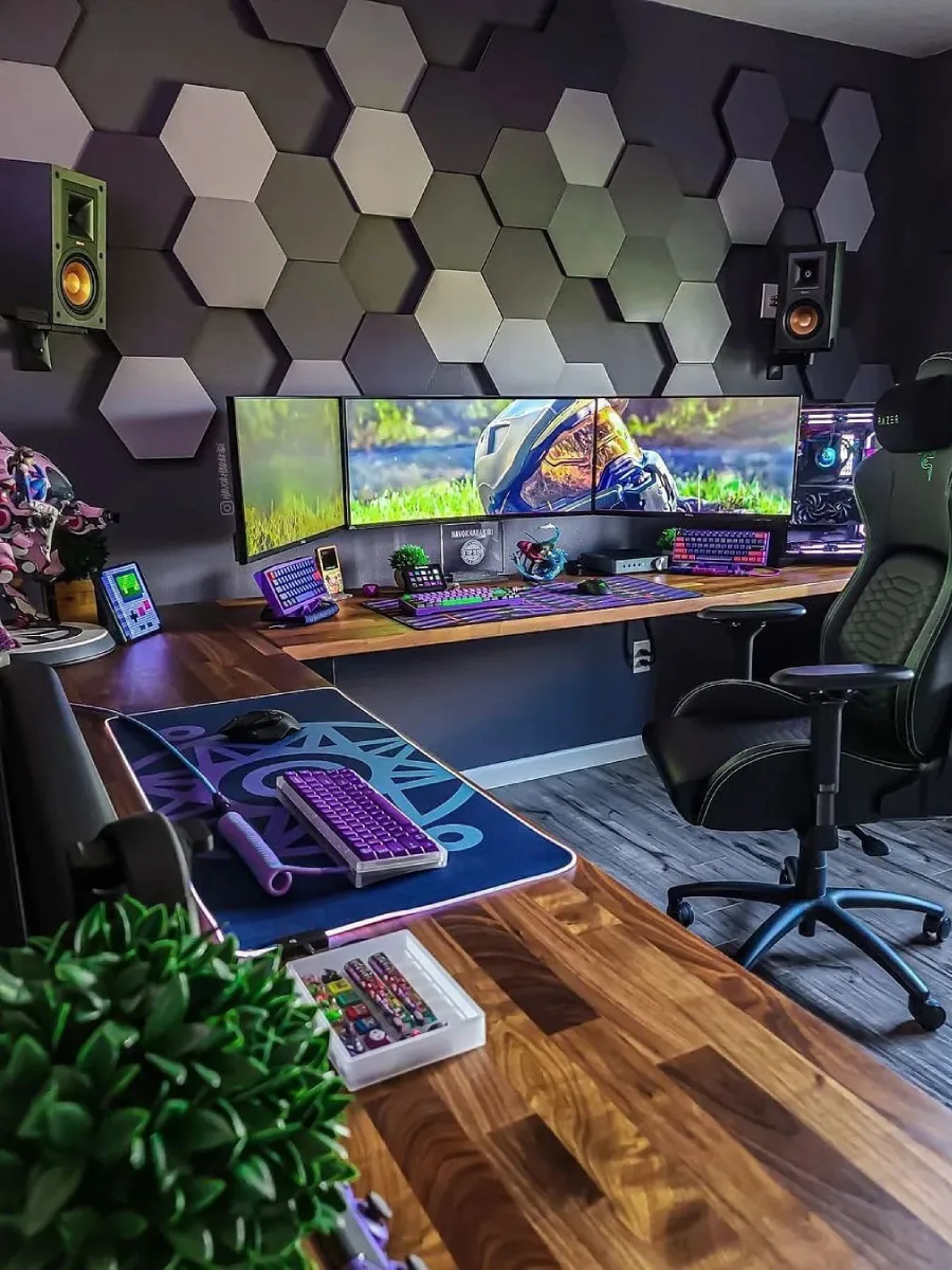 Tampilan jarak dekat setup tiga monitor berjajar yang menampilkan wallpaper helm Master Chief dari game Halo. Terdapat meja kayu, kursi gaming Razer berwarna hitam dan hijau, keyboard mekanik ungu, serta dinding dengan panel heksagonal abu-abu.