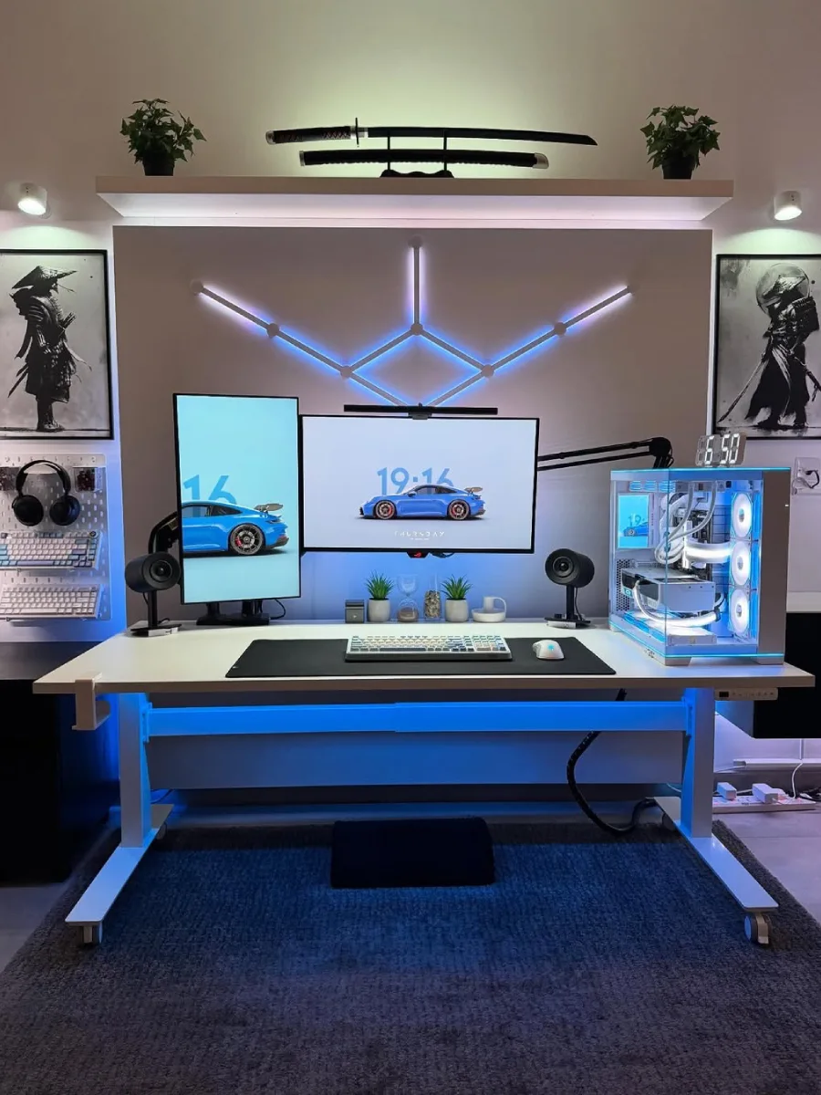 Setup meja kerja minimalis berwarna putih dengan pencahayaan LED biru terang. Terdapat dua monitor (satu horizontal, satu vertikal) menampilkan mobil Porsche biru, PC putih, pajangan dua pedang katana di rak atas, dan dua poster lukisan samurai di dinding kiri dan kanan.