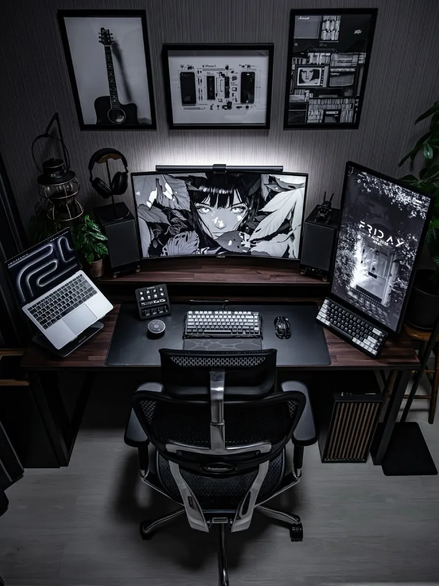 Setup PC gaming bernuansa gelap dan elegan dengan meja kayu. Dilengkapi monitor ultrawide melengkung dan monitor vertikal ber-wallpaper monokrom anime, laptop di dudukan, kursi ergonomis hitam, dan bingkai gambar bertema teknologi di dinding.