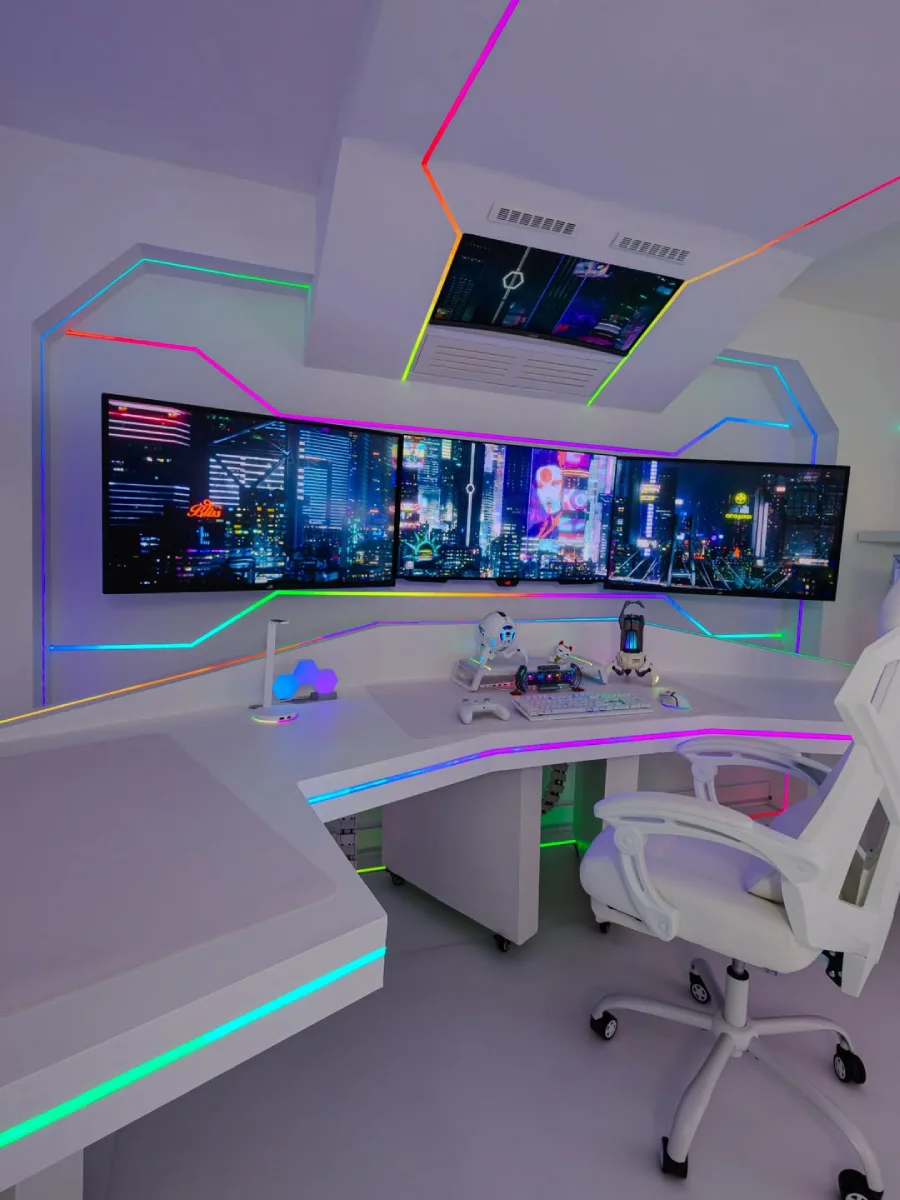 Tampilan luas dari setup PC gaming futuristik serba putih. Menampilkan meja menyudut dengan tiga monitor berlayar cyberpunk, monitor terpasang di langit-langit berdesain geometris, dan pencahayaan RGB yang tertanam di dinding serta tepi meja.