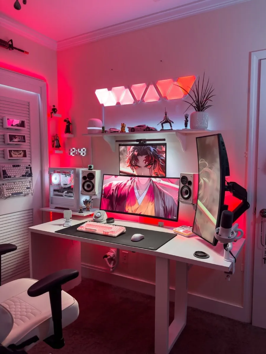 Setup PC gaming dengan pencahayaan LED dominan merah dan merah muda. Terdapat tiga monitor (dua ditumpuk horizontal, satu vertikal di kanan) dengan wallpaper anime Demon Slayer. Meja, casing PC, dan kursi berwarna putih, dilengkapi rak berisi action figure dan lampu dinding segitiga.