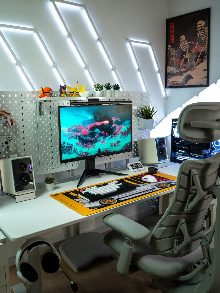 Setup meja komputer bertema putih terang dengan garis-garis lampu LED miring di dinding. Terdapat satu monitor dengan wallpaper naga, pegboard putih yang dihiasi figur Pokémon, desk mat kuning menyala bertema mobil, casing PC, dan kursi ergonomis berwarna abu-abu.