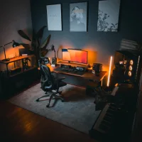 Setup home office minimalis modern dengan meja kayu, monitor widescreen, kursi ergonomis, dan lampu LED warm di ruangan bernuansa gelap.