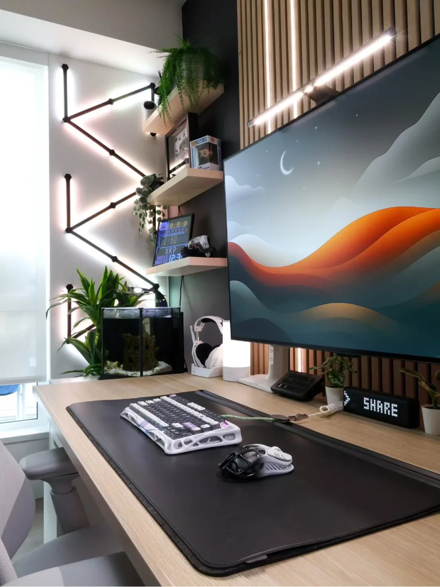 Detail atas meja kerja minimalis modern yang menampilkan keyboard mekanikal putih, mouse berdesain unik, dan akuarium mini di samping monitor.