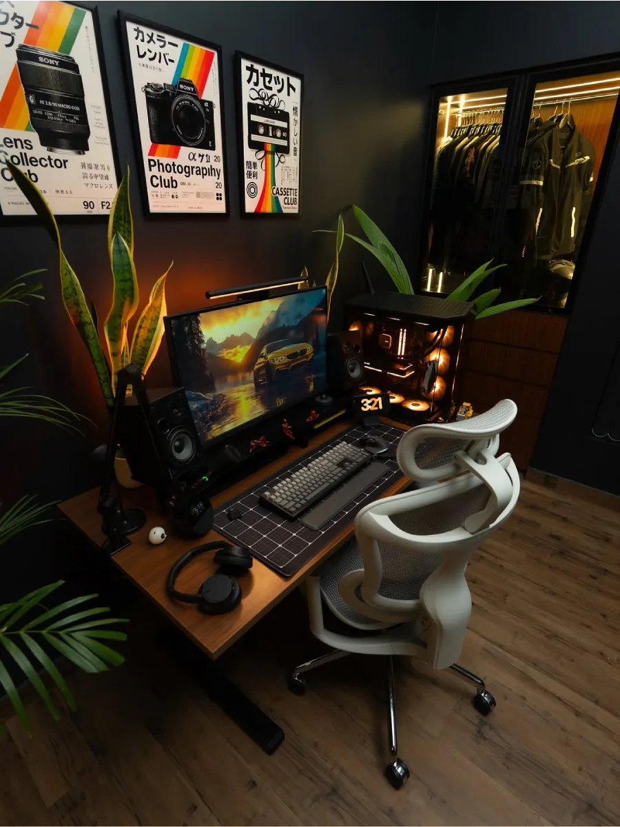 Sudut ruang kerja modern bertema dark room dengan kursi kantor ergonomis putih yang kontras, meja kayu luas, dan lemari pakaian kaca dengan pencahayaan internal.