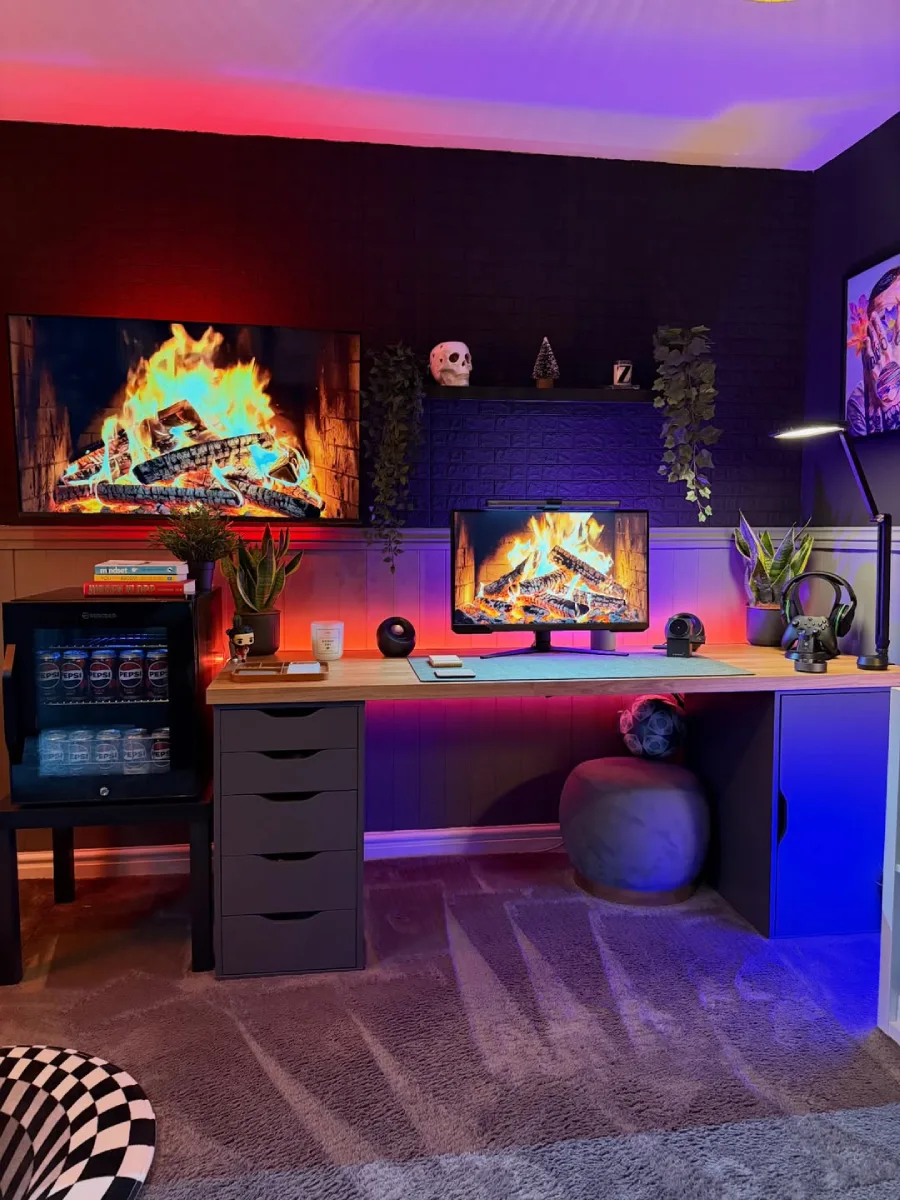 Suasana malam di home office modern dengan pencahayaan ambient RGB perpaduan merah dan biru, monitor dan TV menampilkan visual perapian, menciptakan kesan hangat dan nyaman.