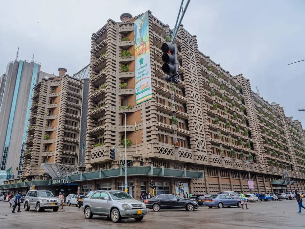 Pemandangan tingkat jalan dari kompleks kantor dan perbelanjaan Eastgate Centre yang khas dan bertekstur di Harare, Zimbabwe, menampilkan fasad dengan sirip dan balkon kecil peneduh matahari yang meniru struktur sarang rayap, di sepanjang jalan kota yang sibuk.