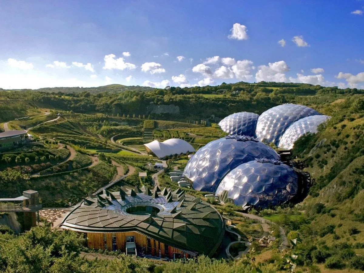 Foto udara lanskap luas memandang melintasi lubang tambang reklamasi bertingkat di Cornwall, yang berisi beberapa biome geodesik raksasa yang saling terhubung dari Proyek Eden, dengan struktur kubah mirip gelembung yang jelas di bawah langit berawan sebagian.