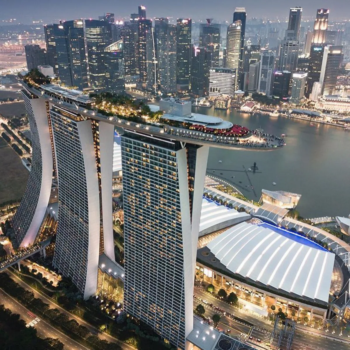 tampilan udara Marina Bay Sands di Singapura saat senja, tiga menara hotel dengan kolam renang tanpa batas di SkyPark berbentuk kapal