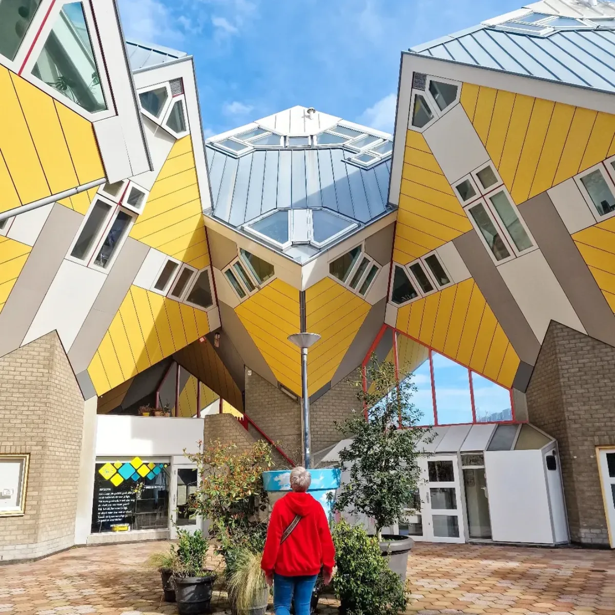 Cube Houses deretan rumah berbentuk kubus berwarna kuning dan putih yang dimiringkan dan ditopang oleh struktur tiang di area pejalan kaki