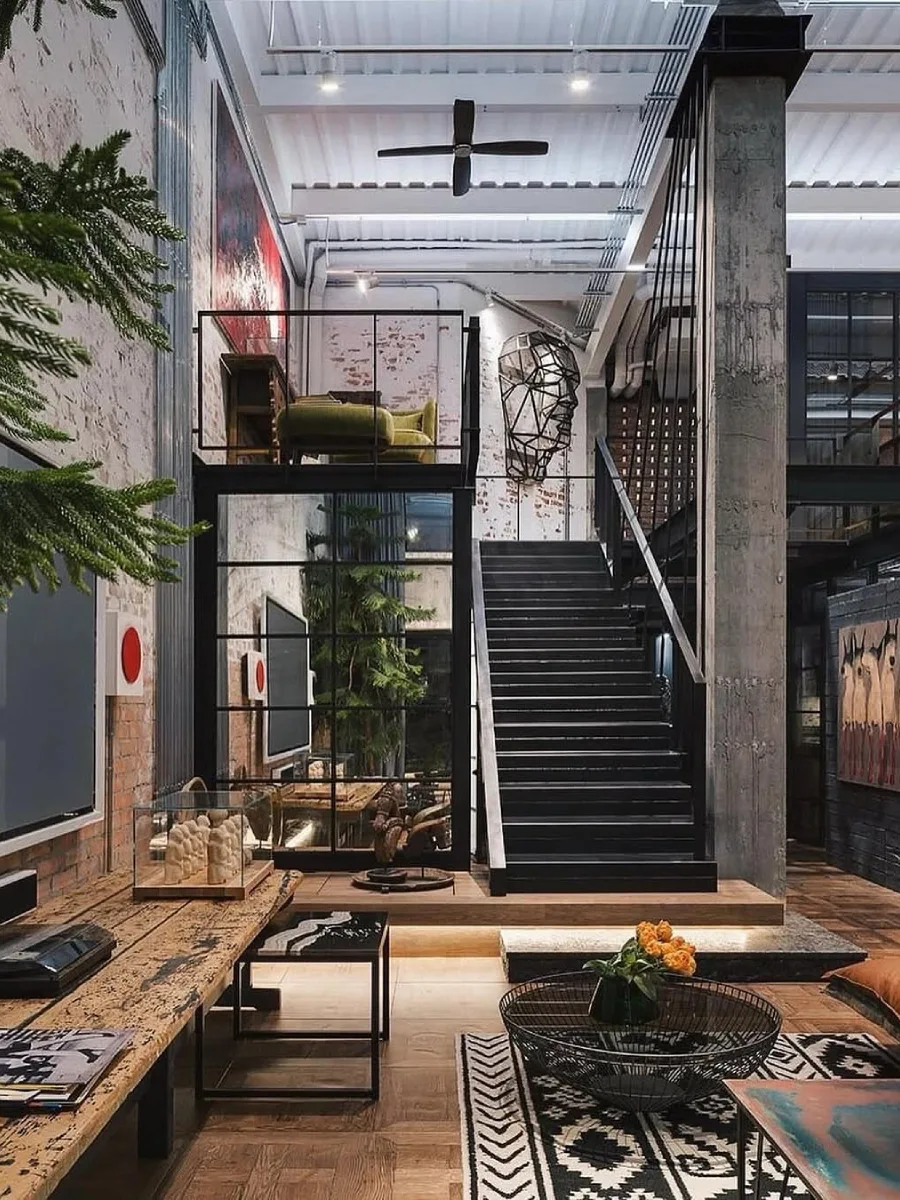 Tangga besi hitam menuju mezzanine di ruangan industrial dengan dinding bata putih ekspos dan dekorasi rangka kepala