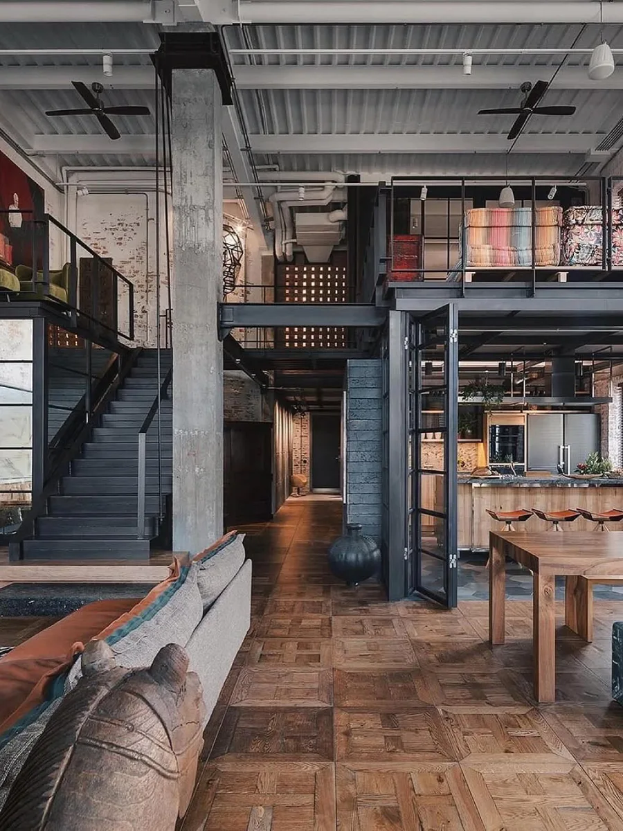 Area makan dan lorong rumah industrial dengan meja kayu solid, lantai parket kayu, dan pilar beton ekspos