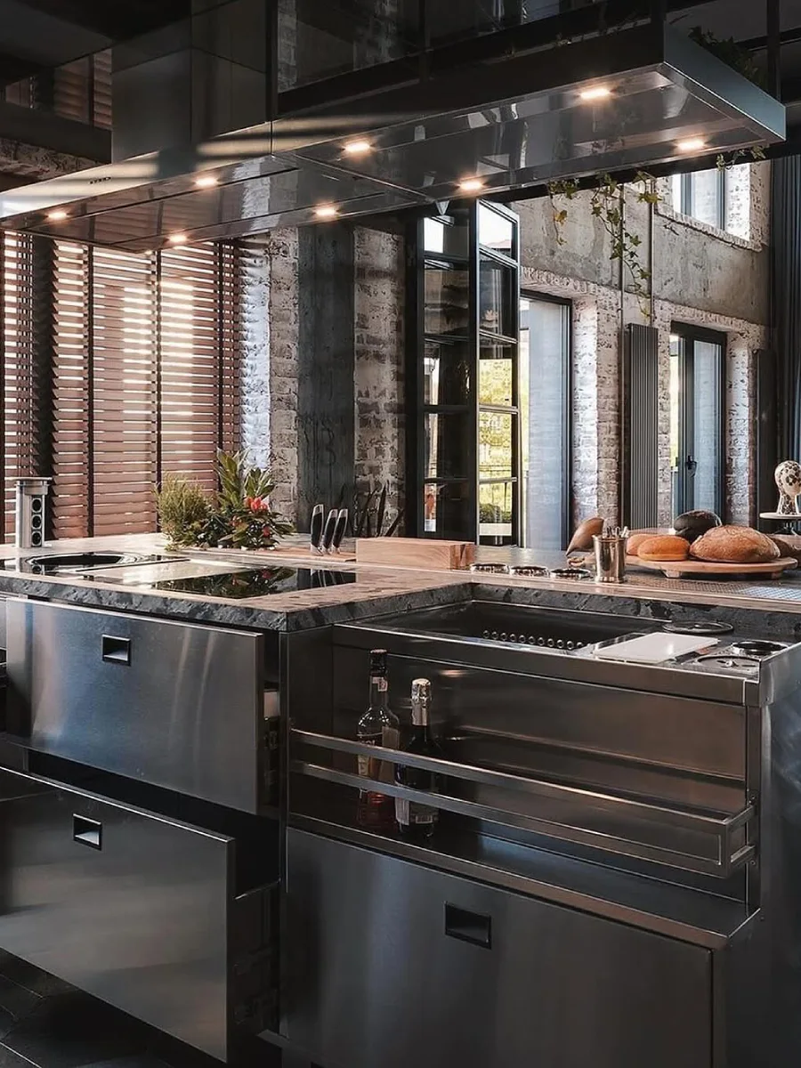 Kabinet meja dapur berbahan stainless steel dalam ruangan bertema industrial dengan latar belakang dinding bata ekspos