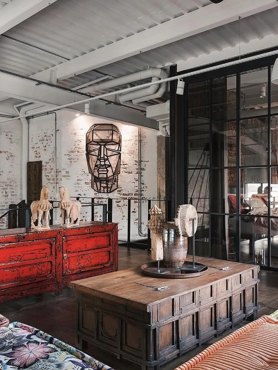 Area santai mezzanine bernuansa industrial dengan dinding bata cat putih, meja peti kayu rustic, dan kabinet merah antik