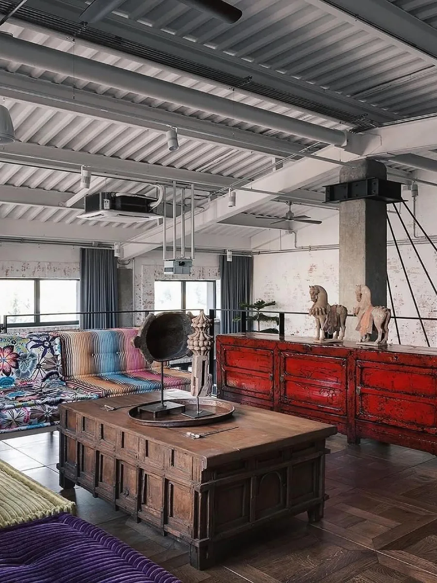 Plafon metal bergelombang bercat putih dengan pipa ekspos di area mezzanine industrial yang dilengkapi bantalan duduk bermotif warna-warni