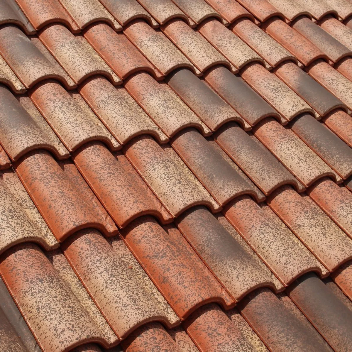 Susunan rapat genteng tanah liat tradisional berwarna merah terakota dengan corak alami kehitaman pada permukaannya
