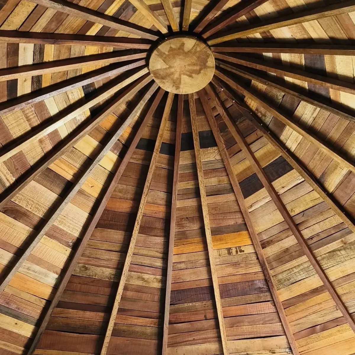 Pemandangan dari bawah ke atas yang memperlihatkan detail struktur rangka dan susunan panel kayu pada atap berbentuk melingkar atau kerucut