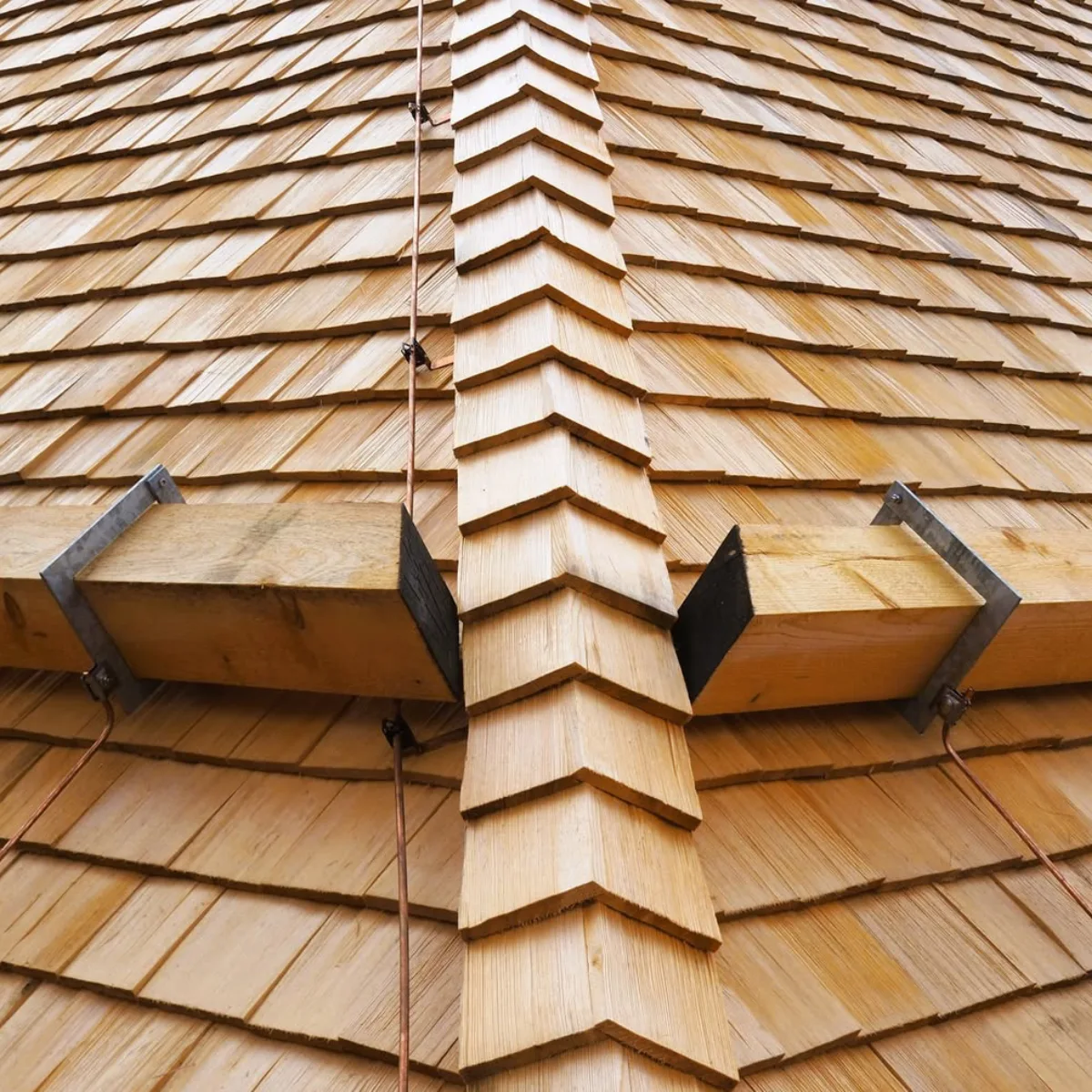 Tampilan dekat detail atap sirap kayu yang tersusun rapi dengan bagian bubungan (nok) di tengah, serta dilengkapi balok penyangga kayu dan sistem kabel tembaga.