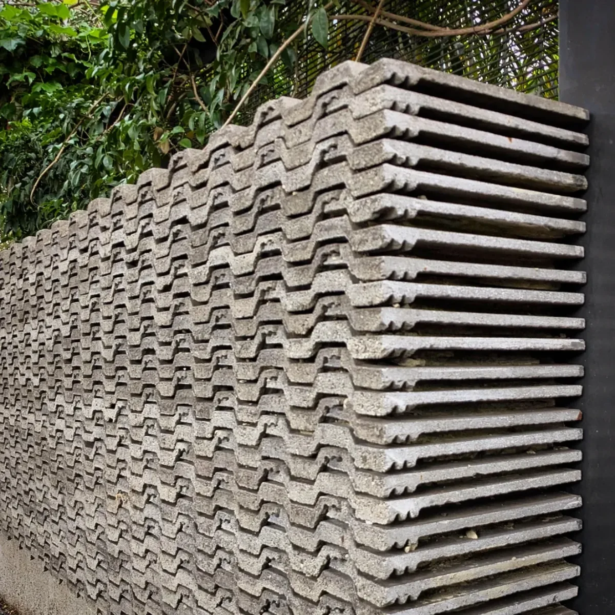 Tumpukan tinggi genteng beton tebal berwarna abu-abu dengan profil bergelombang yang tersusun rapi