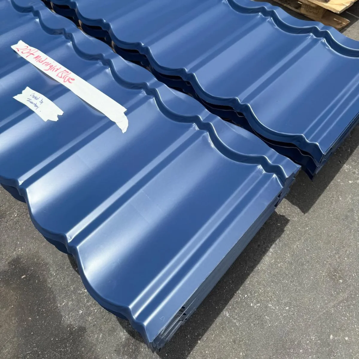 Tumpukan genteng metal polos berwarna biru tua yang tersusun rapi di atas palet kayu
