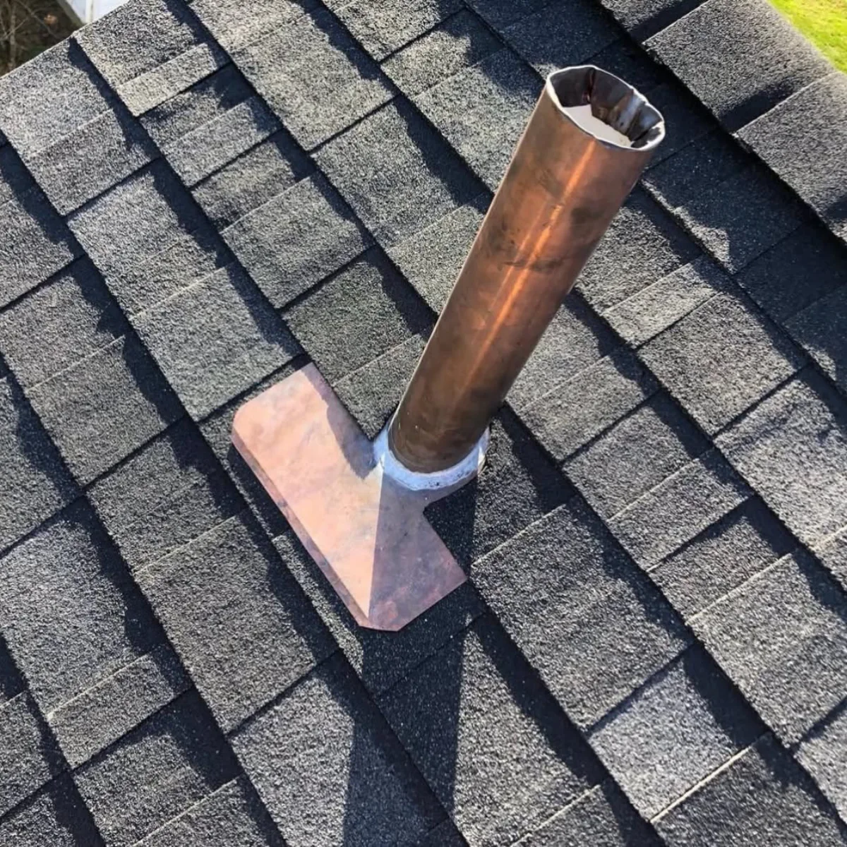 Detail permukaan atap aspal bitumen bertekstur warna hitam keabuan dengan pelat tembaga dan pipa menembus atap