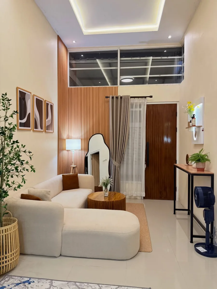 Ruang tamu berkonsep Japandi dengan sofa modular berwarna krem, meja kopi kayu bergaris vertikal, cermin lantai bergelombang, dan aksen dinding panel kayu.