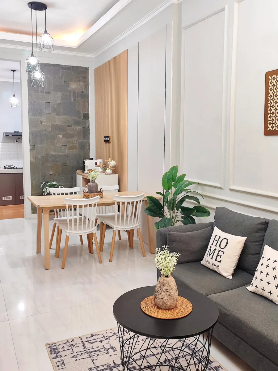 Ruang keluarga berkonsep terbuka dengan sofa abu-abu, meja makan kayu bergaya Skandinavia, dan area pembuat kopi berlatar panel kayu.